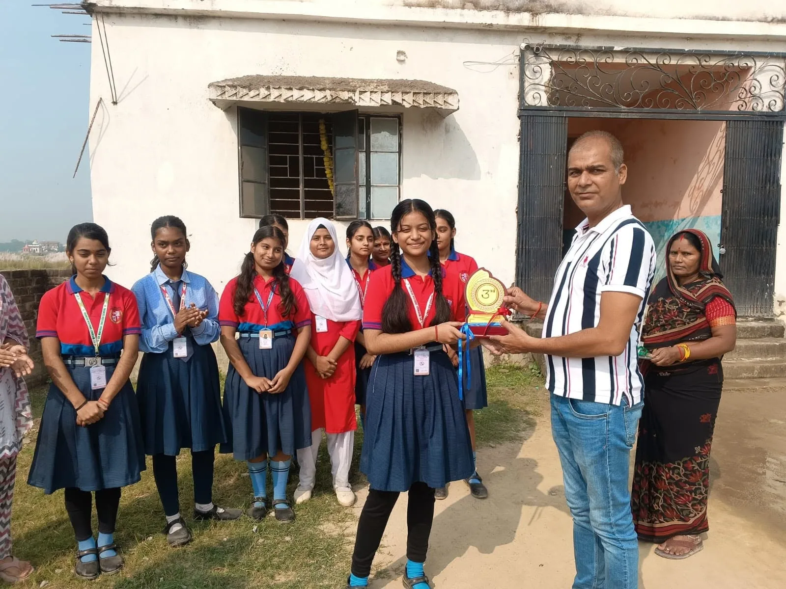 A group of students being presented with an award by a member of staff outside the school