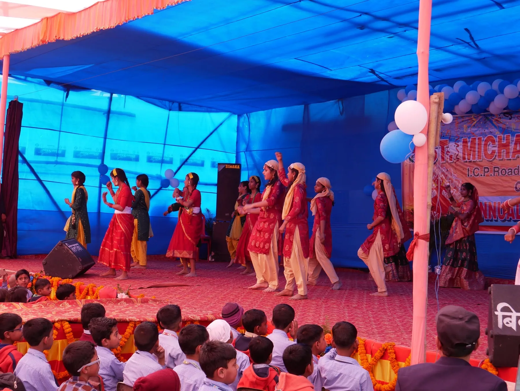 Students performing a group dance on a lit stage in front of a seated audience